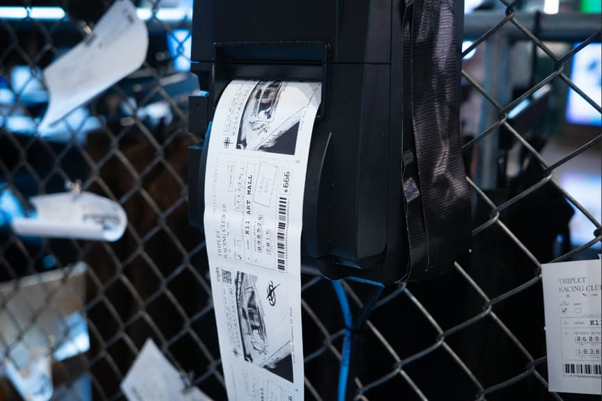 A printed speeding-ticket style photo slip hanging from a chain-link fence.