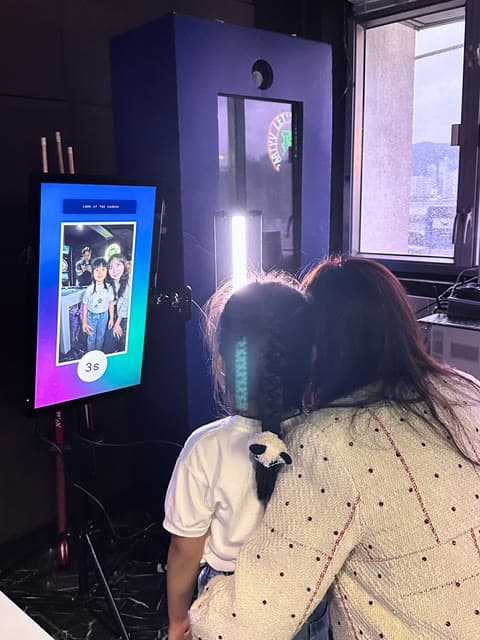 A parent and child watching their photo appear on the booth screen.